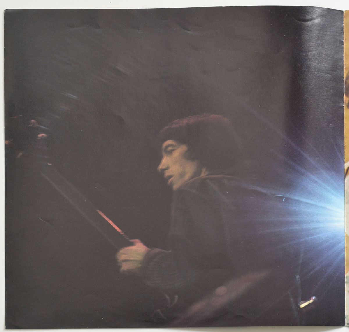 Live stage photo of Bill Wyman from the 1974 German Big Hits booklet, playing bass guitar under low light with a radiant blue lens flare emerging from the right side.
